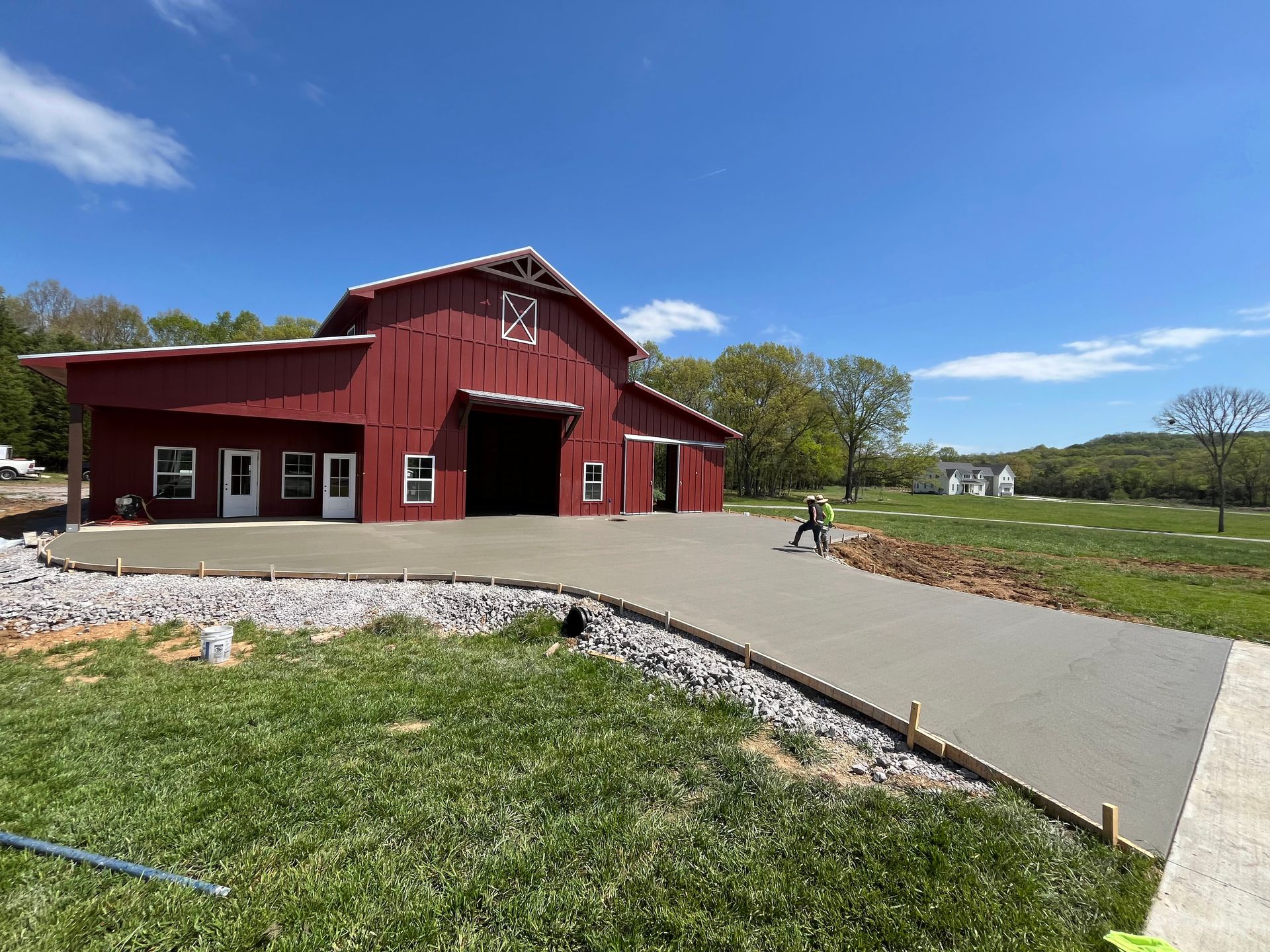 A red barn with a concrete driveway in front of it.