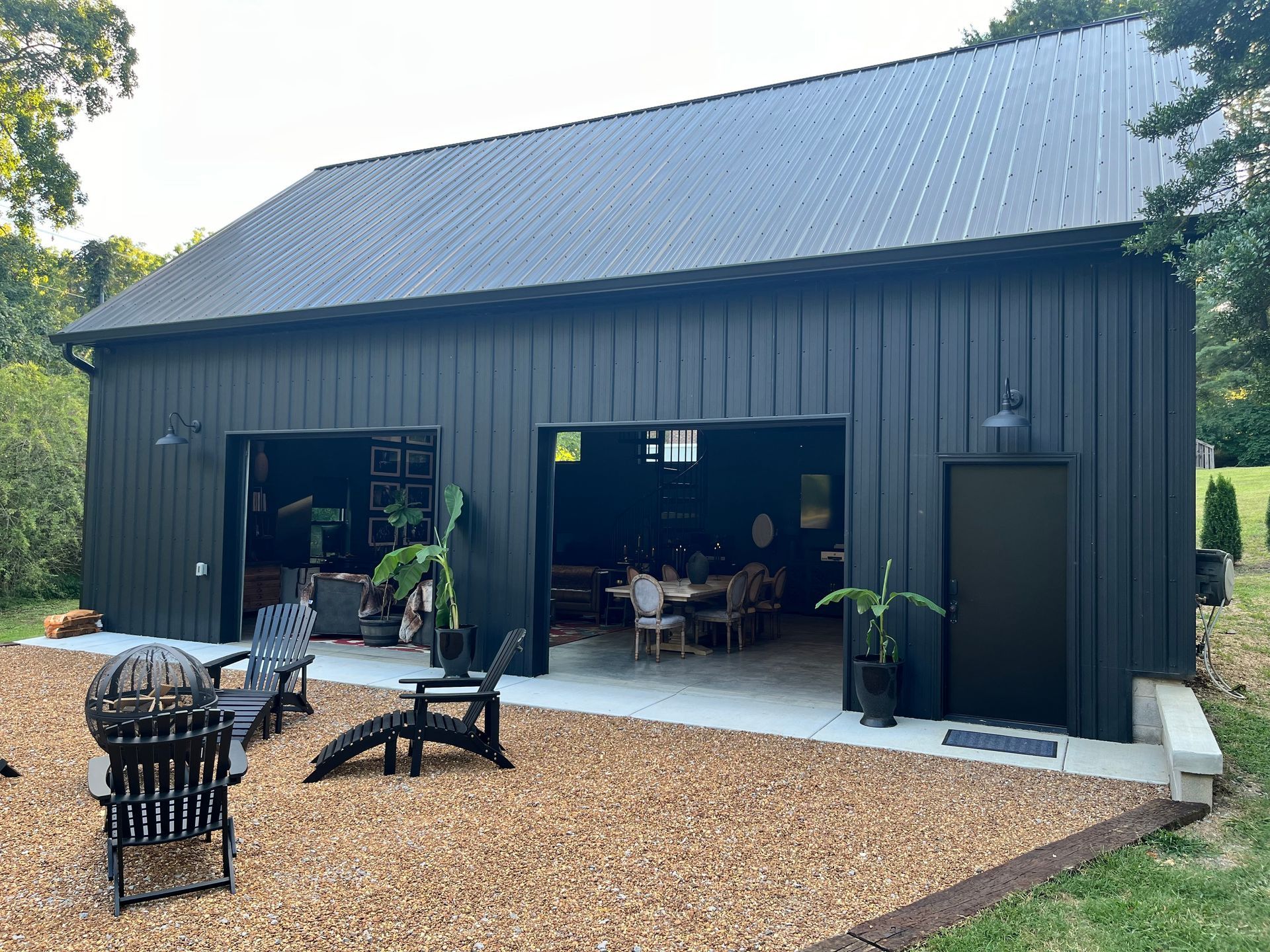 A black barn with its doors open and chairs in front of it.