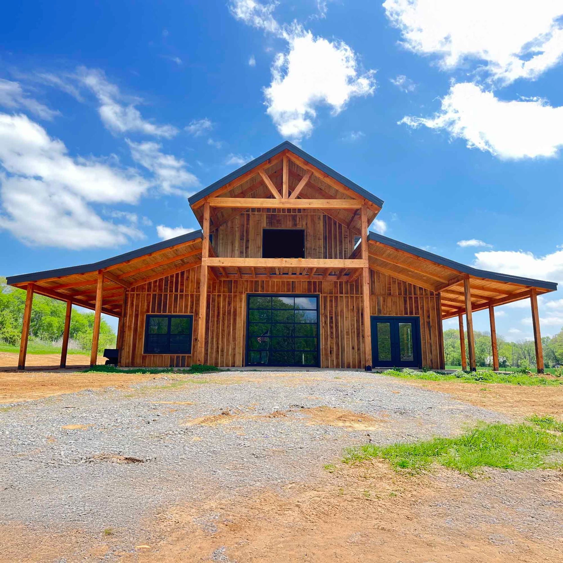 A white barn with a wooden roof and a bell tower is sitting on top of a lush green field.