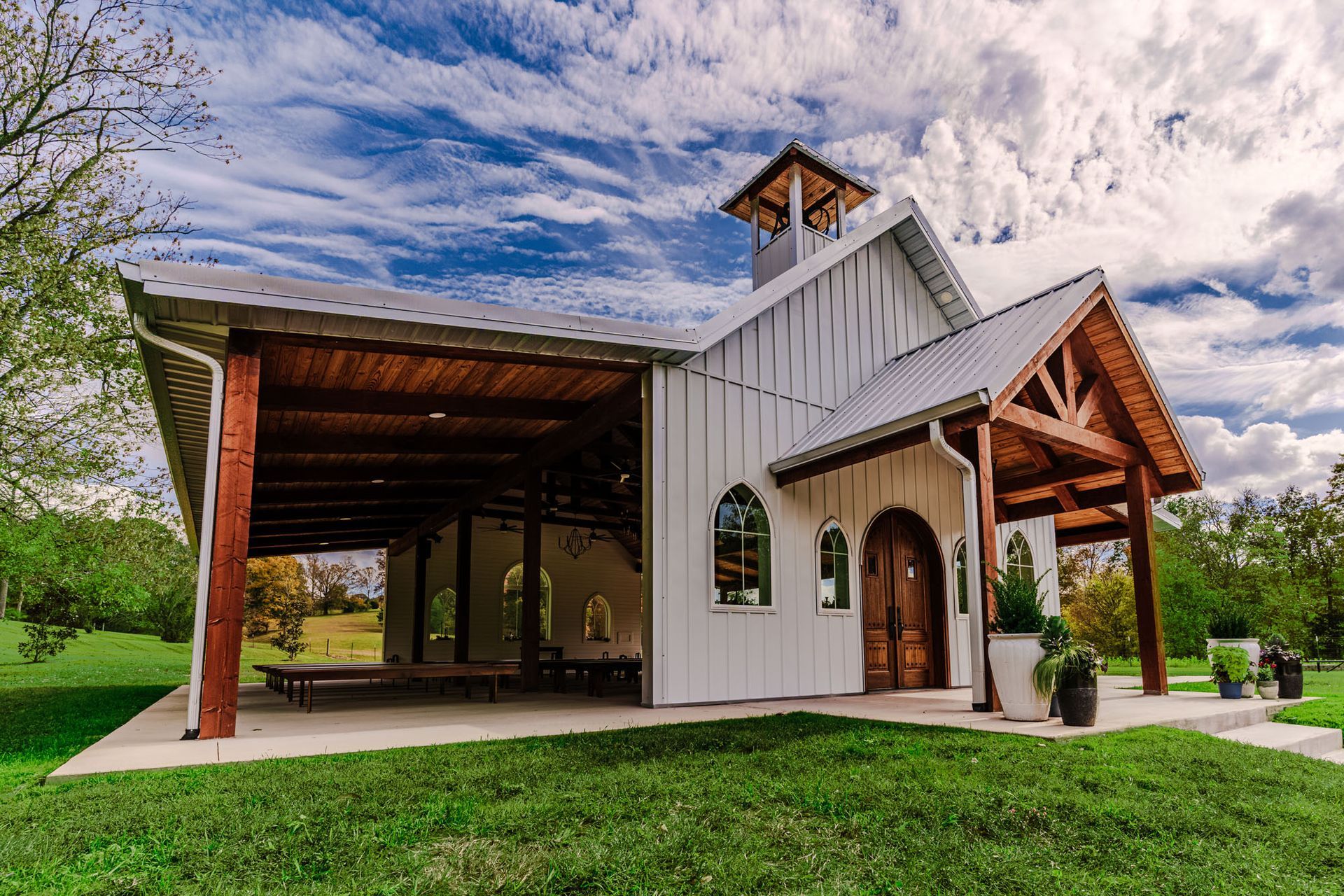 A white barn with a wooden roof and a bell tower is sitting on top of a lush green field.