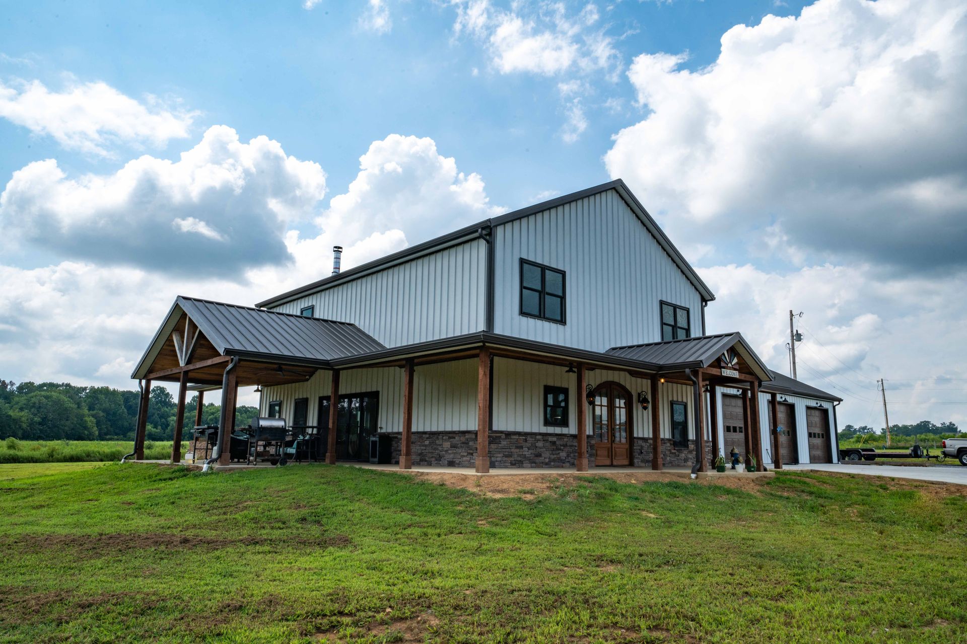 A large white barn with a porch and a truck parked in front of it.