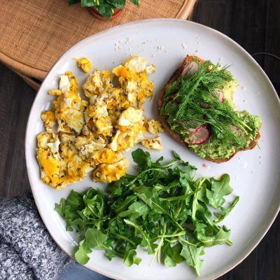 a white plate topped with scrambled eggs and avocado toast .