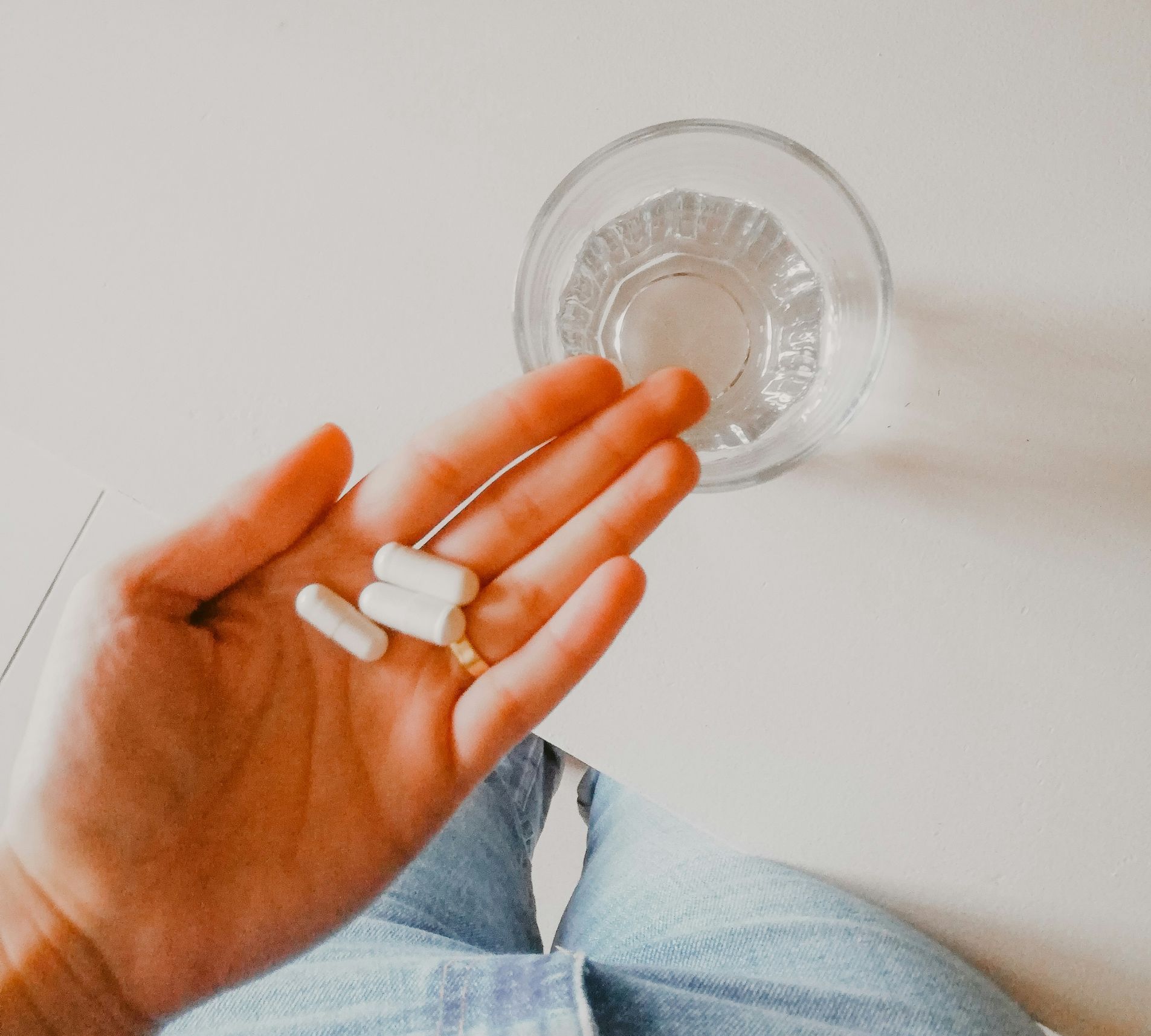 A person is holding pills in their hand next to a glass of water.