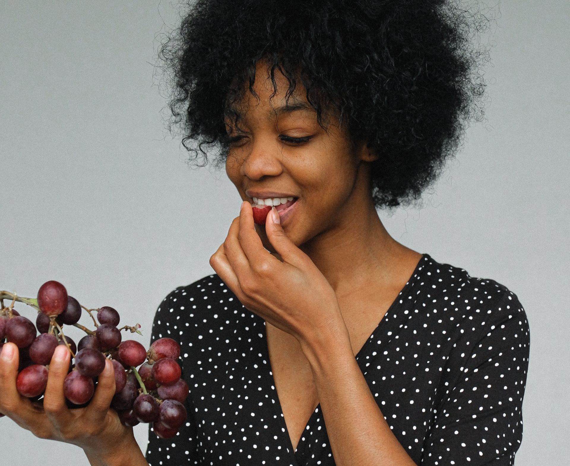 A woman is eating a grape from a bunch of grapes.