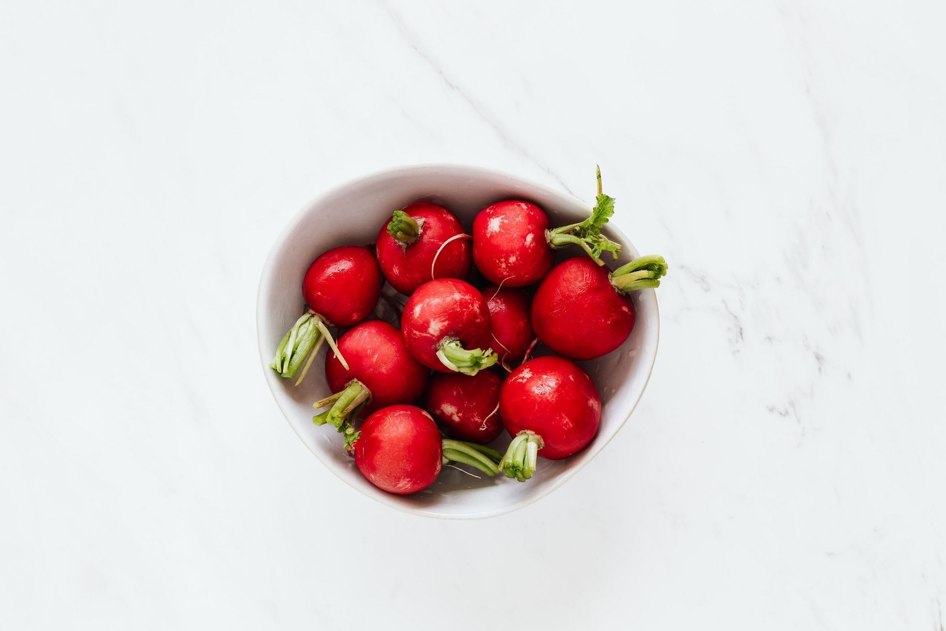 a white bowl filled with red radishes on a white surface .