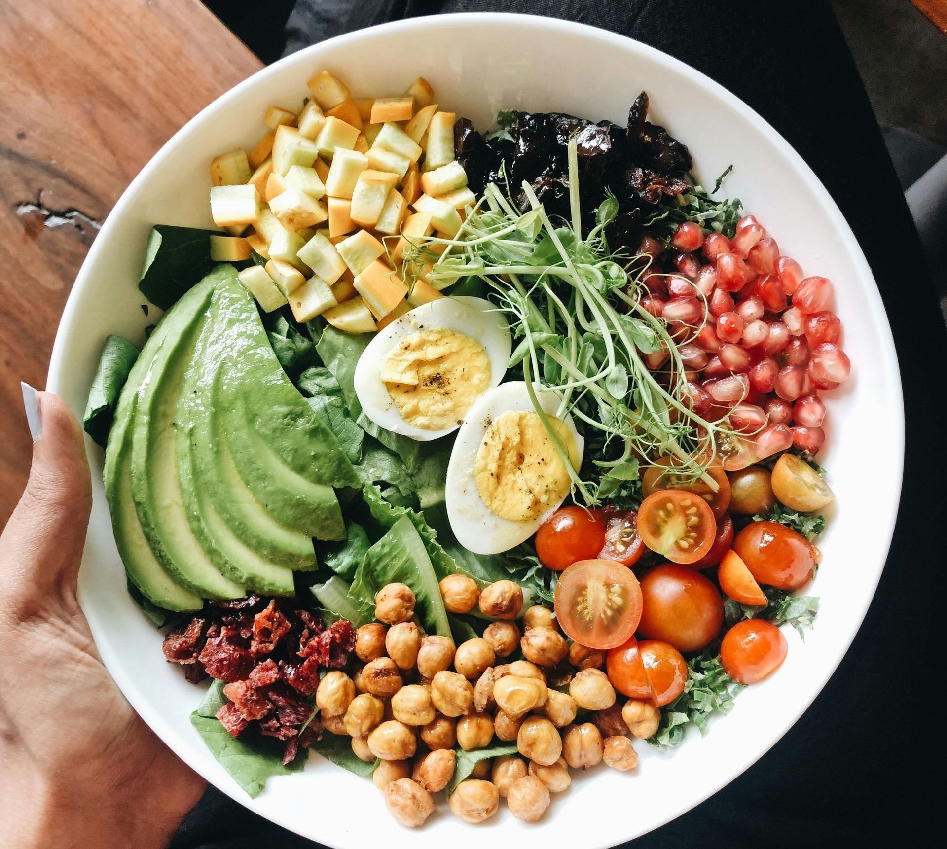 Salad bowl with avocado, chickpeas, eggs, tomatoes, pomegranate seeds, tofu, and sprouts.