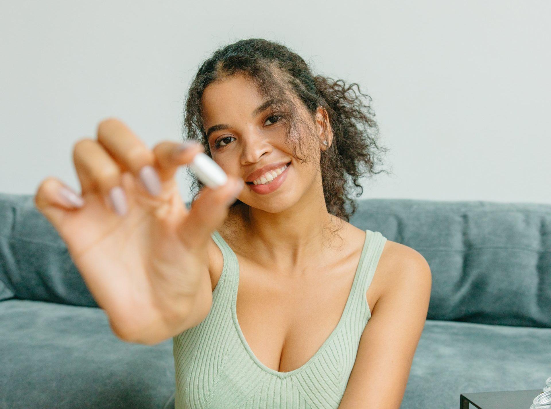 A woman is sitting on a couch holding a pill in her hand.