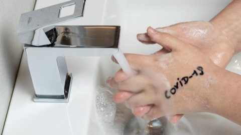 A person is washing their hands in a sink with the word covid-19 written on their hand.