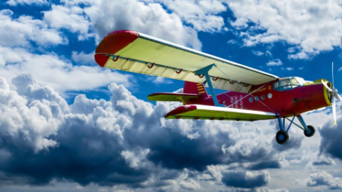 A small red and white plane is flying through the clouds.