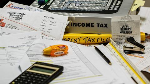 A messy desk with papers , a calculator , and a box that says income tax.