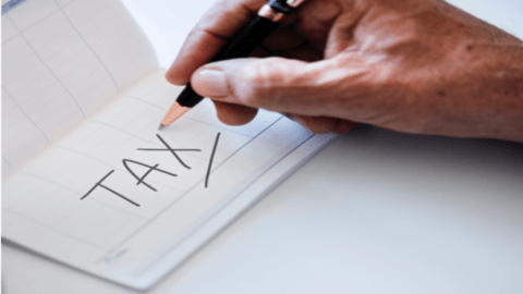 A person is writing the word tax on a check with a pencil.