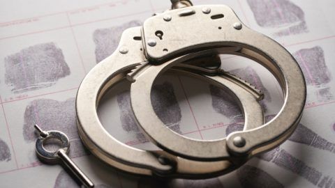 A pair of handcuffs and a key are sitting on top of a piece of paper with fingerprints.