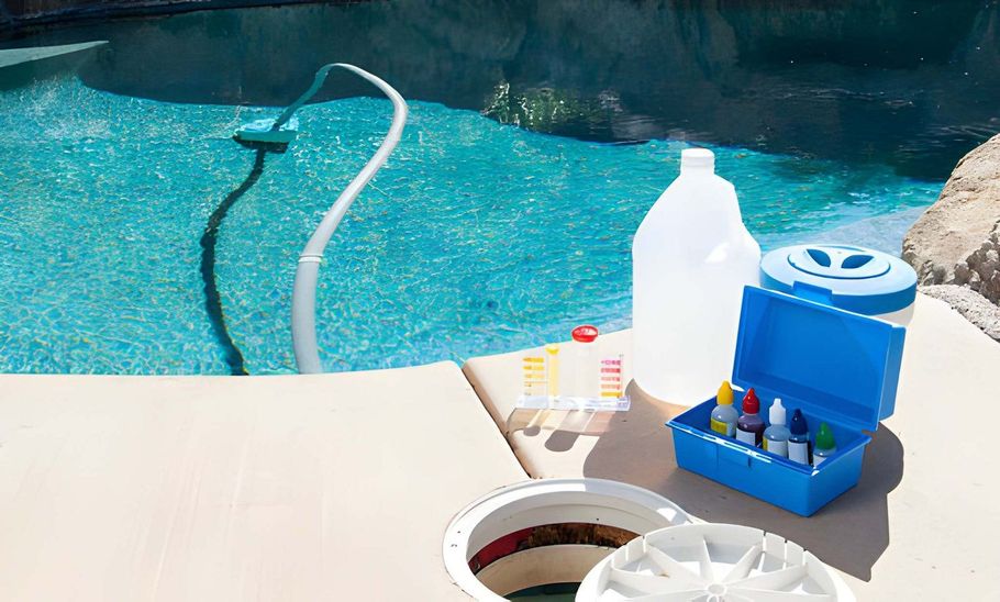 Poolside cleaning supplies beside a blue swimming pool, with hoses and bottles on a patio.