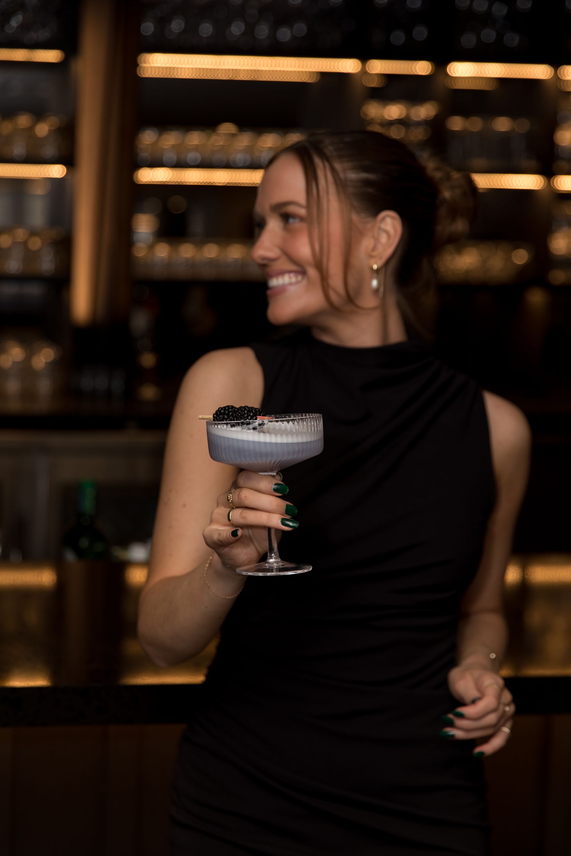 a woman in a black dress is holding a cocktail in her hand .