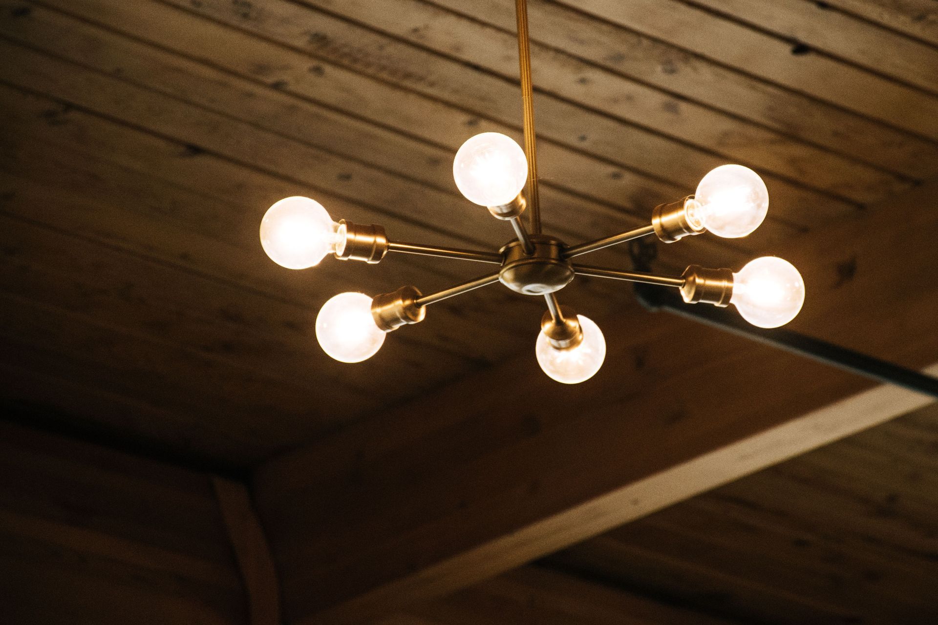 Modern chandelier with lit bulbs hanging from a wooden ceiling