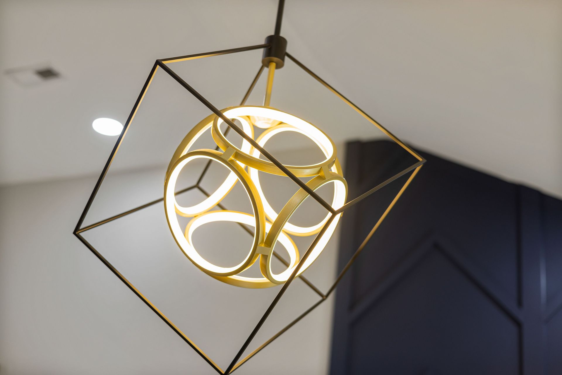 Geometric gold pendant light with a glowing circular center, hanging from the ceiling indoors