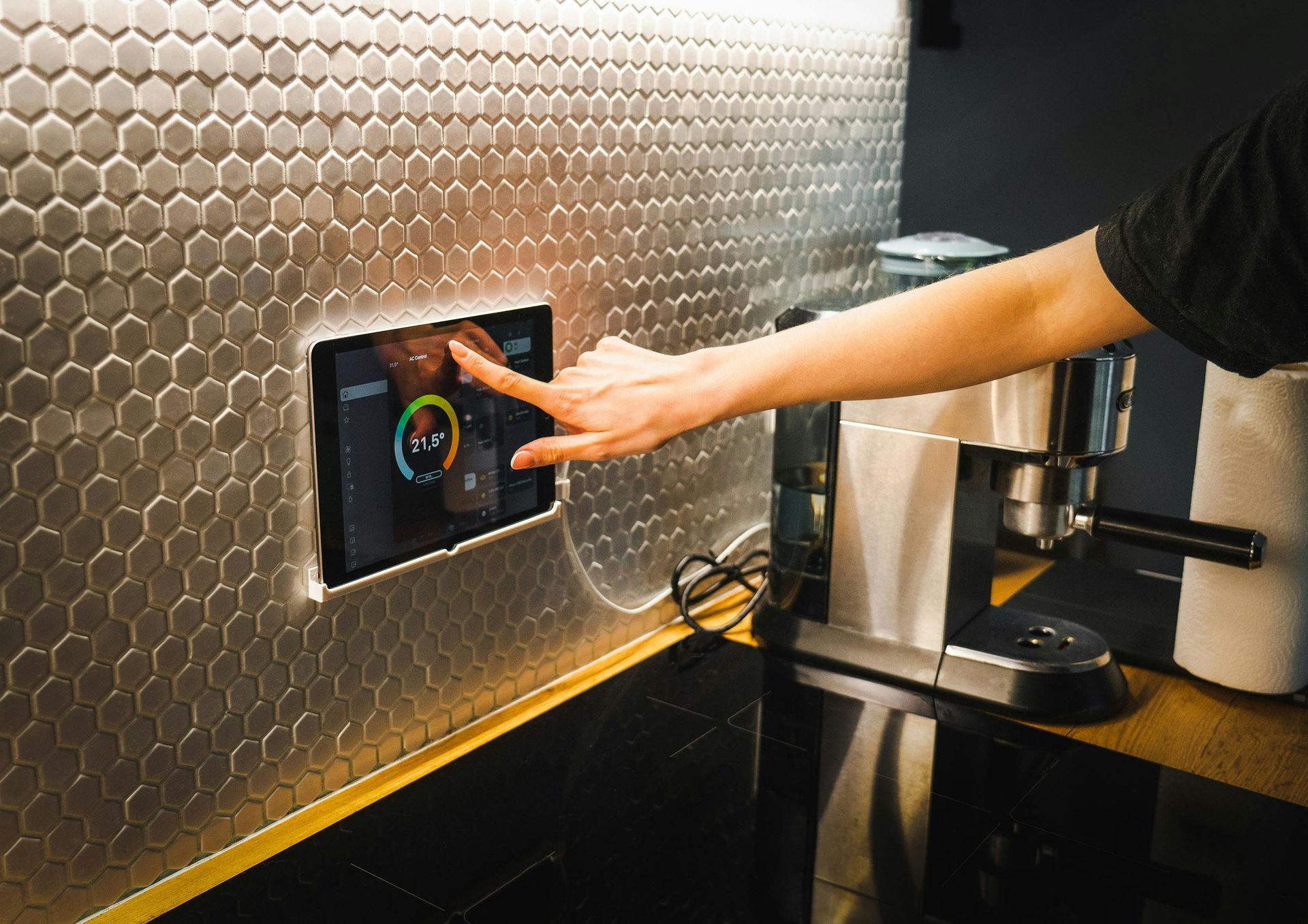 Person pressing a touchscreen on a stainless steel coffee machine in a kitchen.