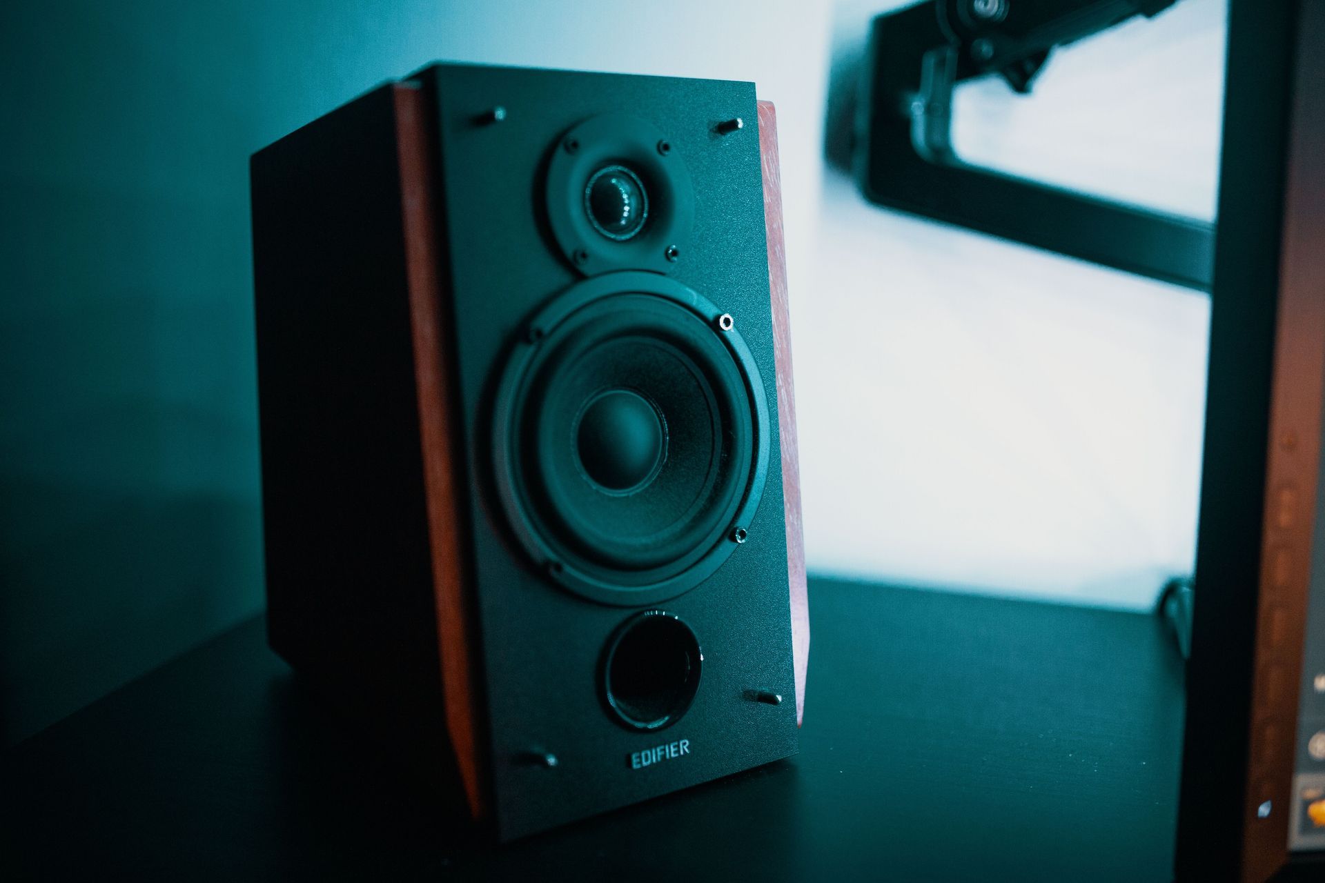 Black speaker on a desk in teal lighting near a bright window