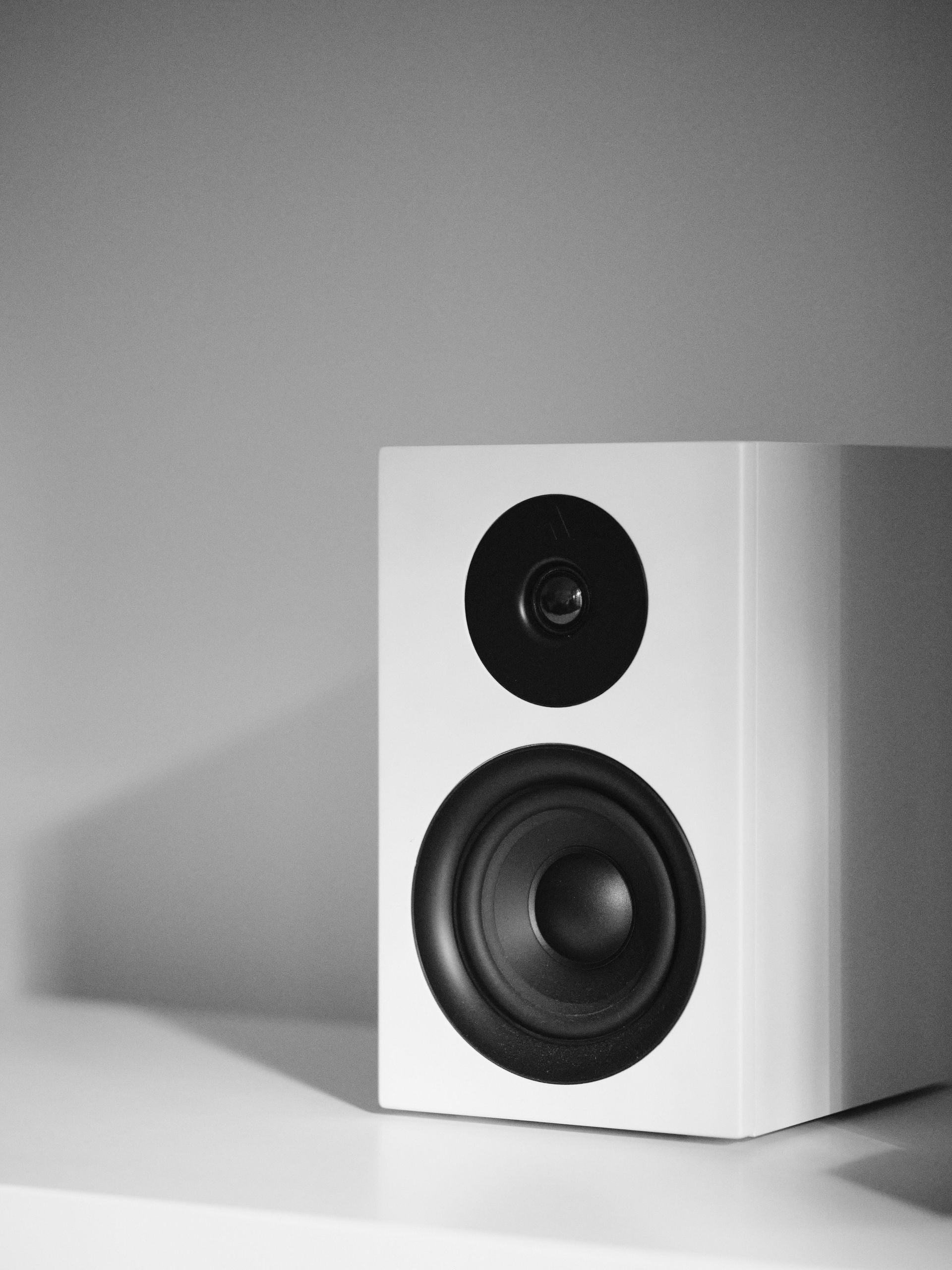 White speaker cabinet with a black tweeter and woofer on a plain background
