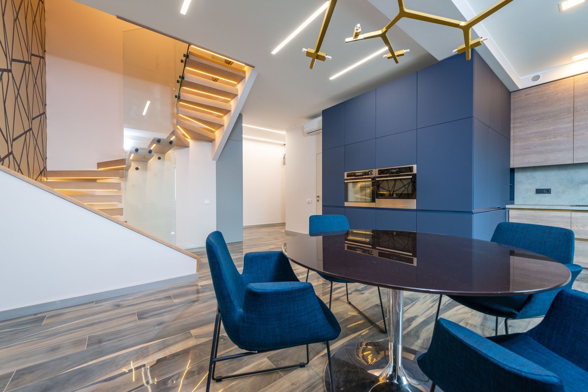 Modern lobby lounge with blue chairs, round table, staircase, and blue accent wall fireplace