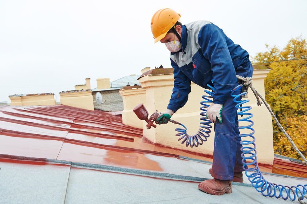 Skilled Roofer Using A Spray Gun To Apply Paint Onto A Metal Roofing Sheet — ACT Roofing in Googong, NSW