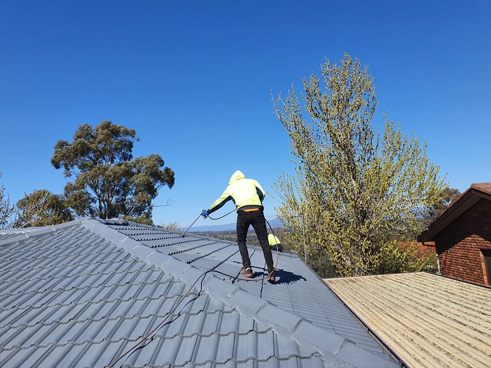 Person Is Spraying Paint On The Roof — ACT Roofing in Ngunnawal, ACT