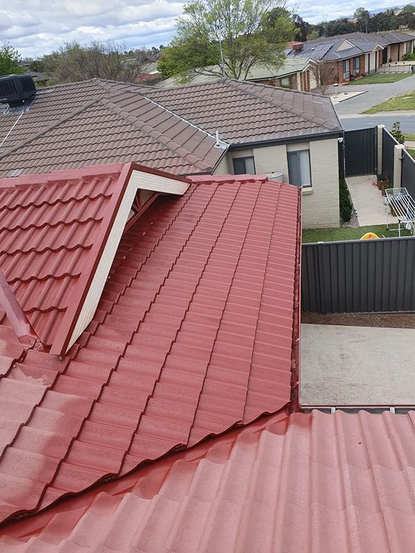 A Red Tiled Roof Is Installed On Top Of A House In A Residential Area — ACT Roofing in Ngunnawal, ACT