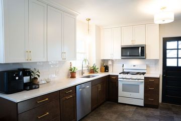 Bright white kitchen with dark lower cabinets, stainless appliances, black countertop, and pendant lights