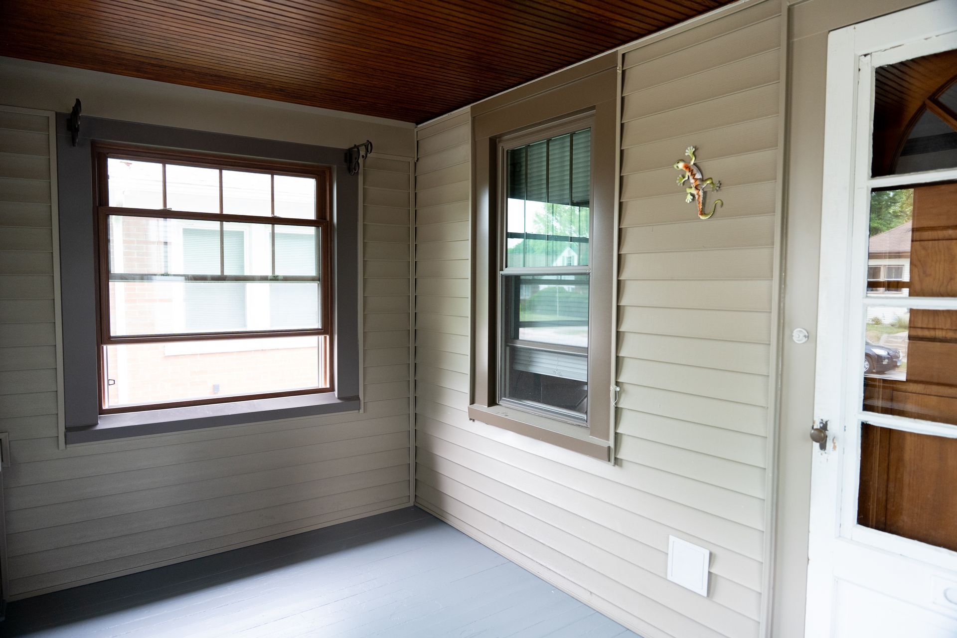 Covered porch with white siding, wood ceiling, window, and white door with screen storm door.