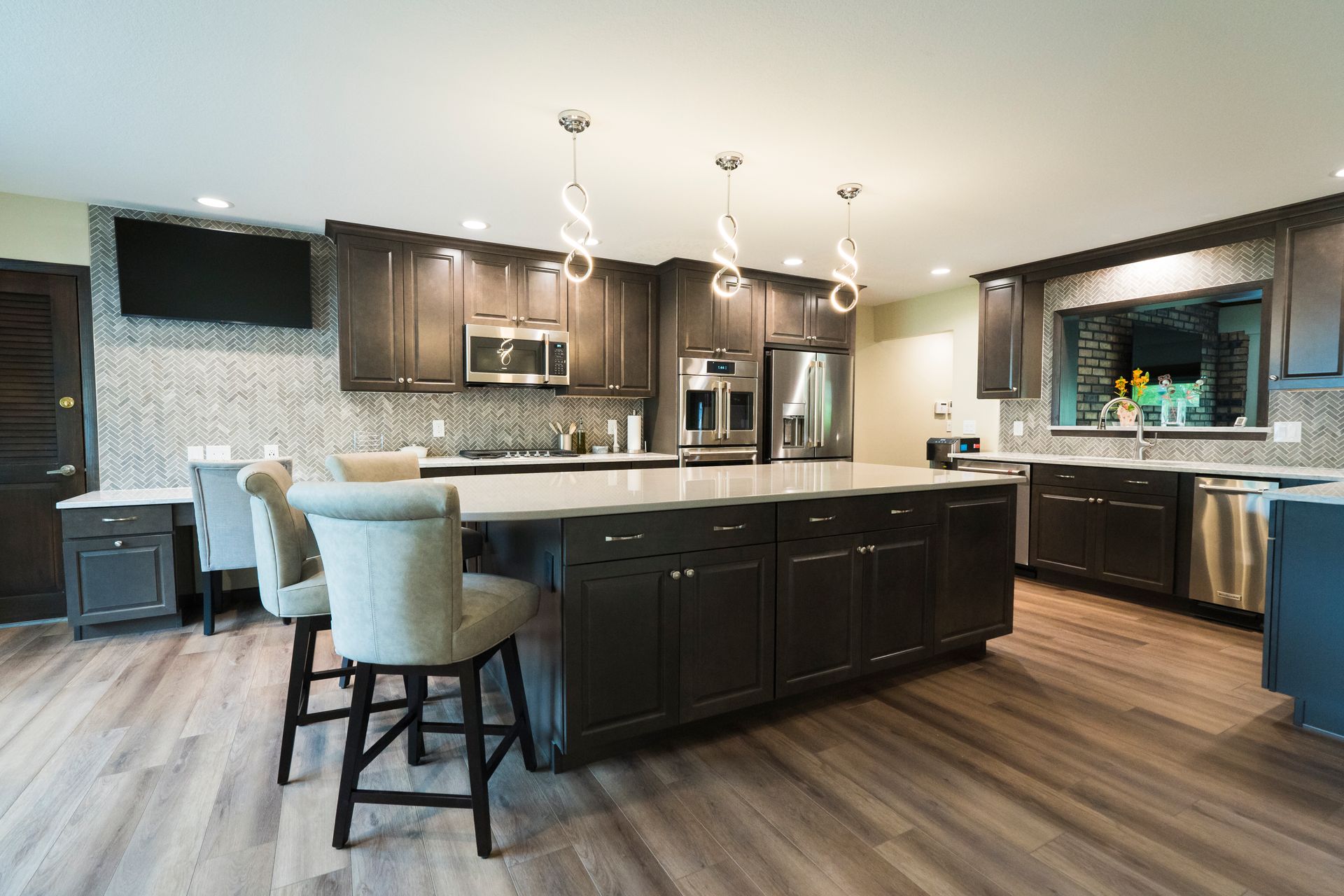 Modern kitchen with dark cabinets, large island, pendant lights, and wood-look flooring