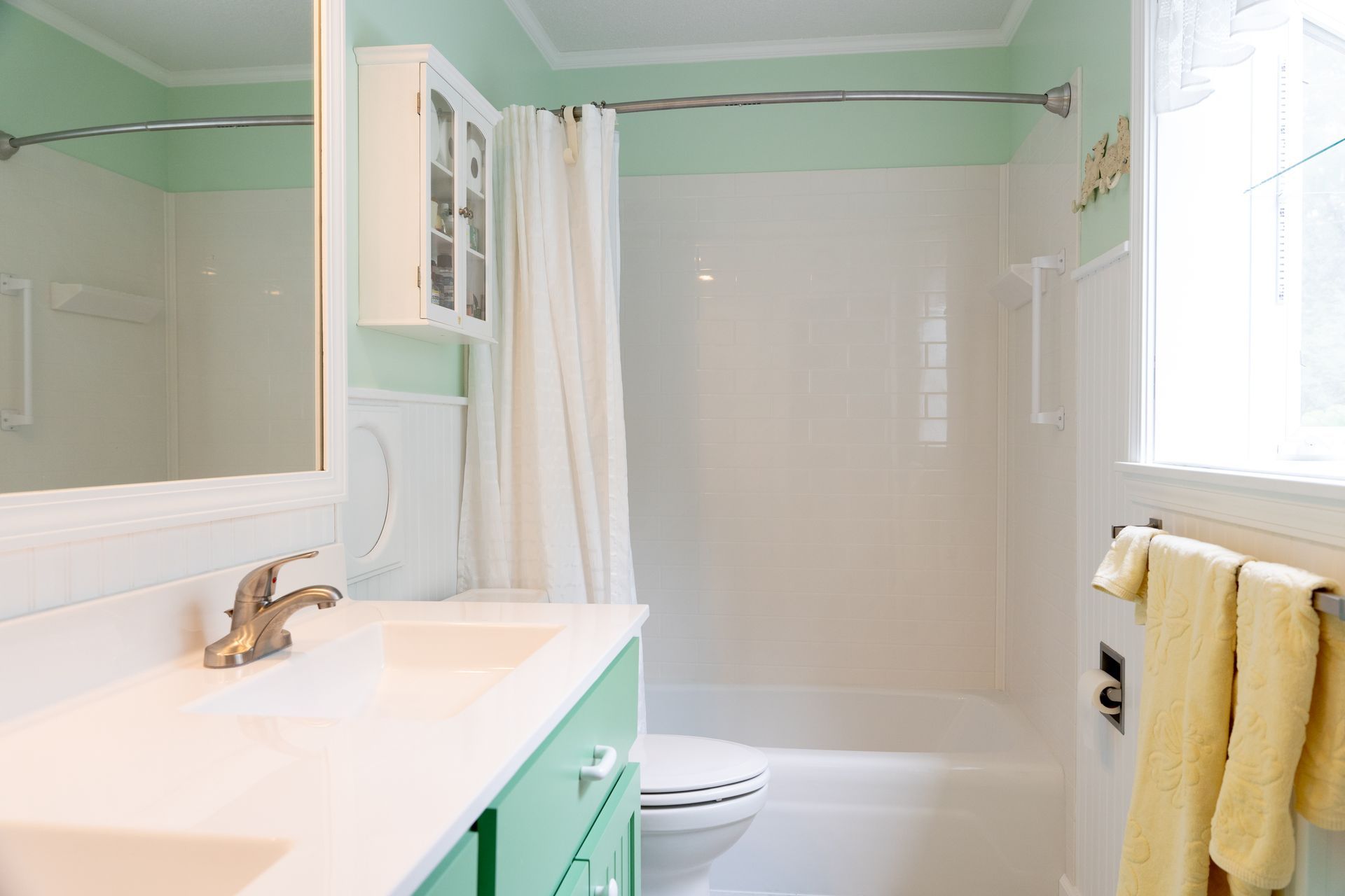 Bright bathroom with mint green walls, white tub and vanity, and yellow towels by a window