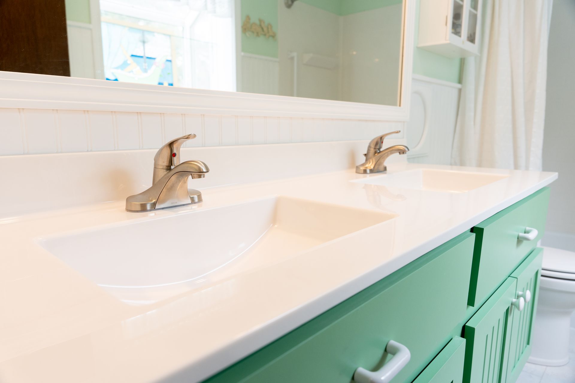 Bright bathroom vanity with twin sinks and chrome faucets, featuring a white countertop and mint-green cabinets