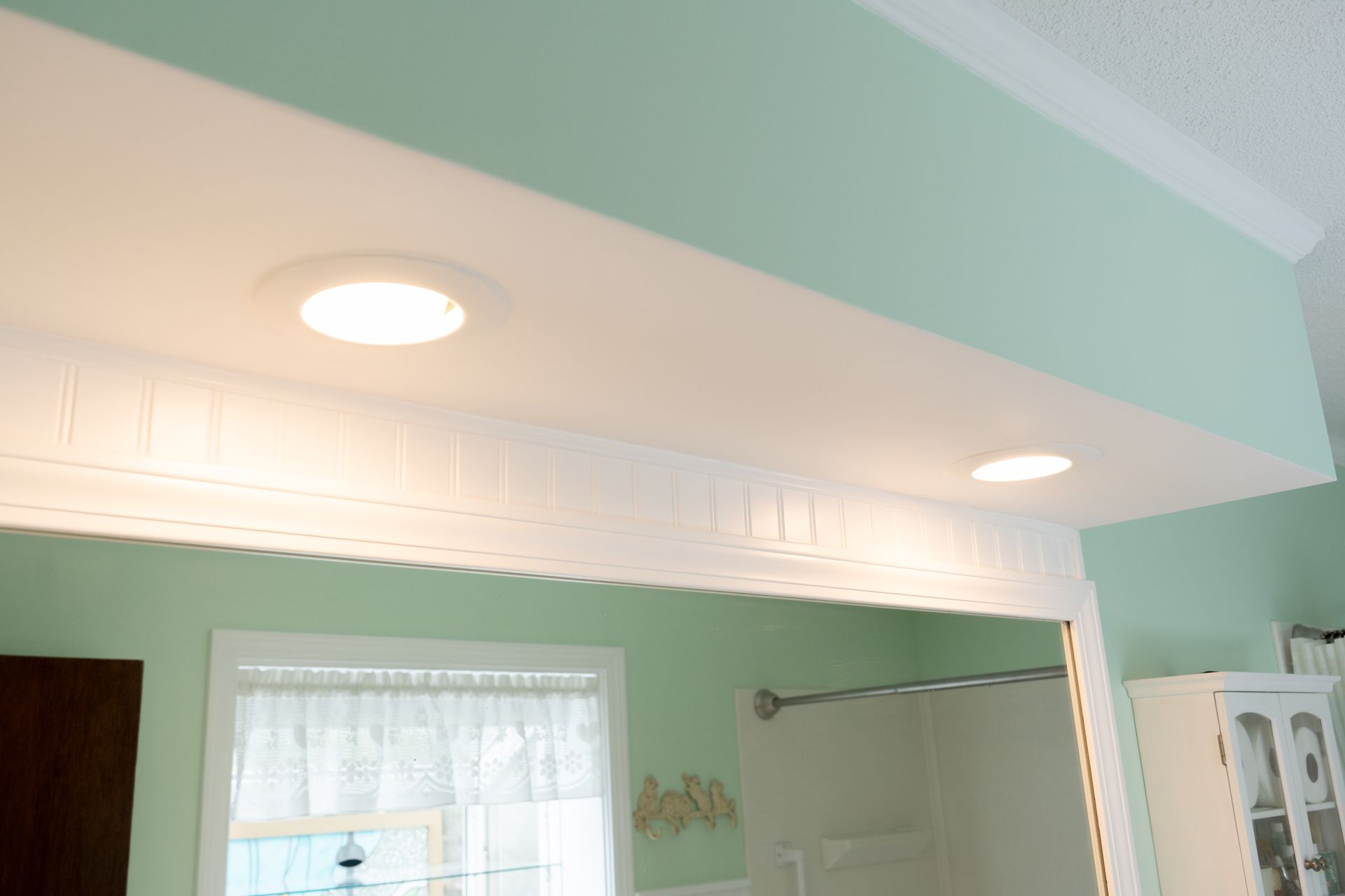 Mint green room with recessed ceiling lights, a window, and a wall-mounted TV above a doorway.