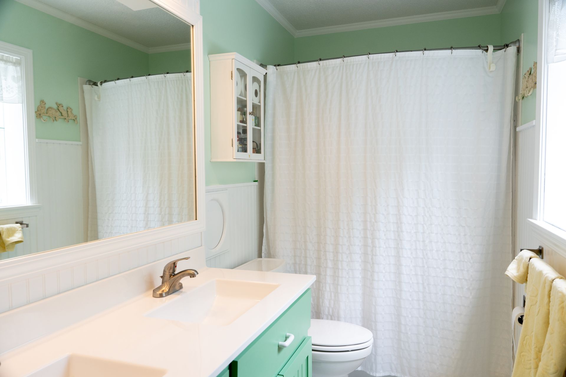 Small mint-green bathroom with white vanity, mirror, shower curtain, and toilet.