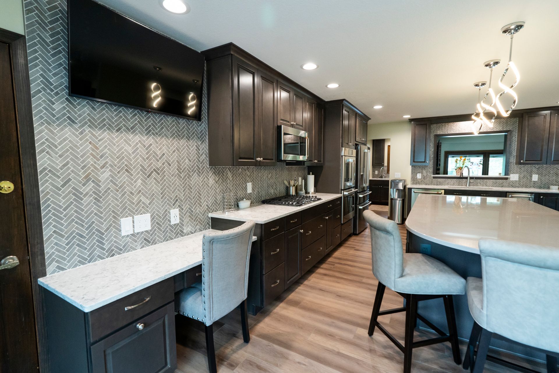 Modern kitchen with dark cabinets, white countertops, bar seating, and wood-look flooring