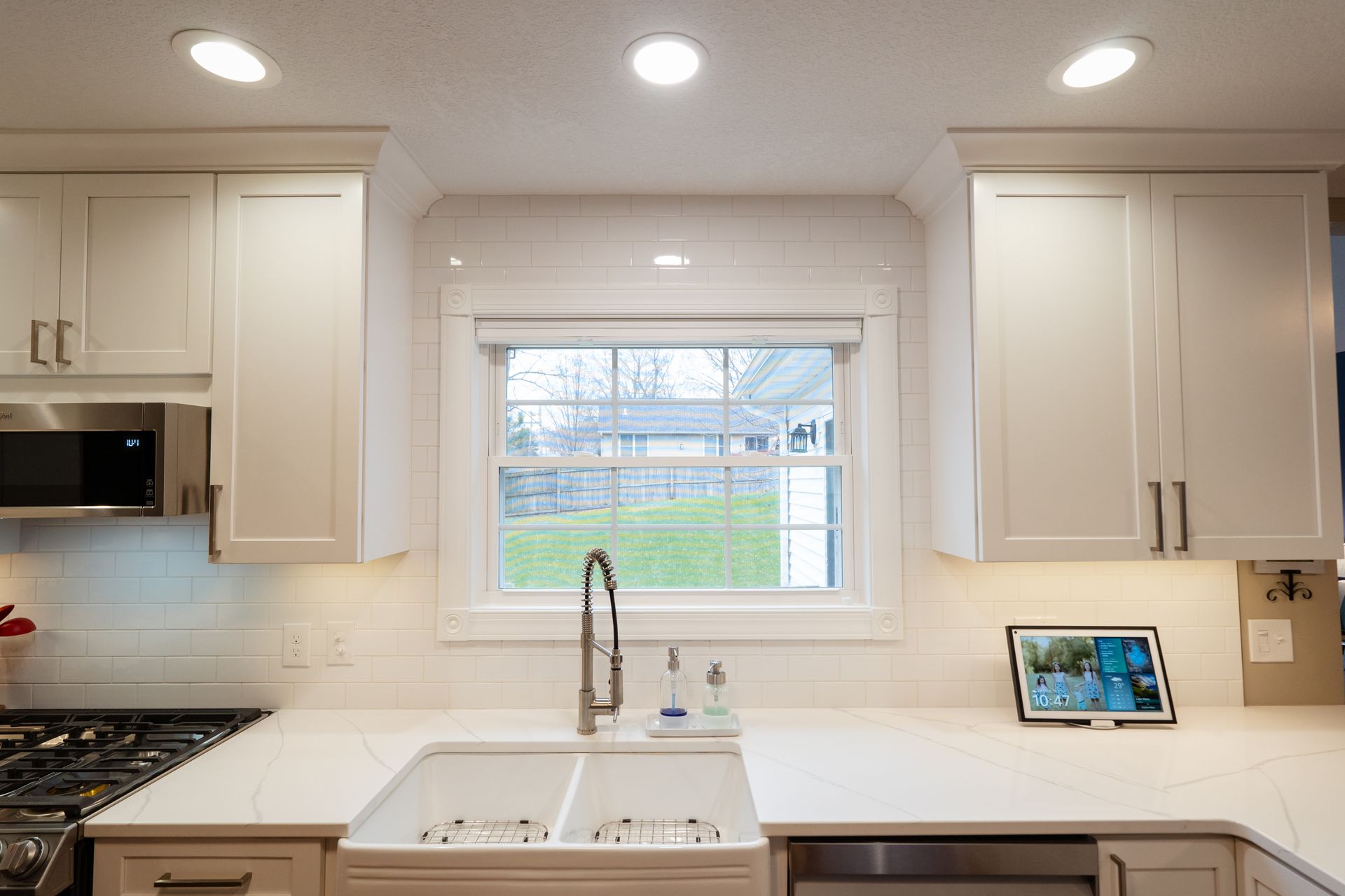 Bright white kitchen with sink under window, cabinets, and a small tablet on the counter.