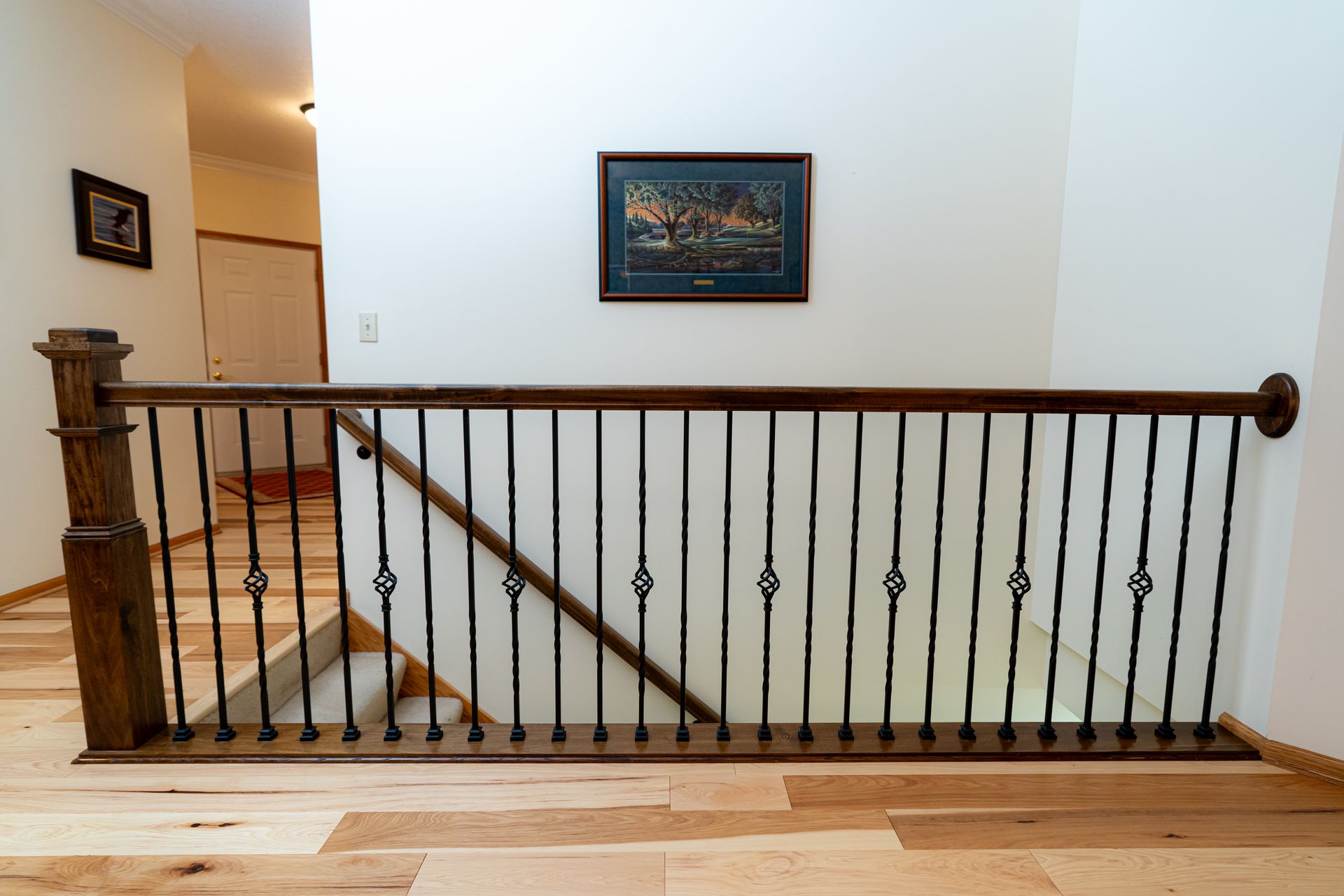 Interior staircase with wooden railing, white walls, and framed artwork above the stairs
