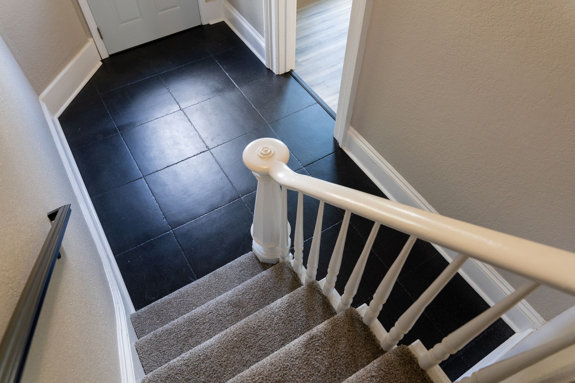 Staircase with gray carpet and white railing leading to a dark tiled hallway with open doors