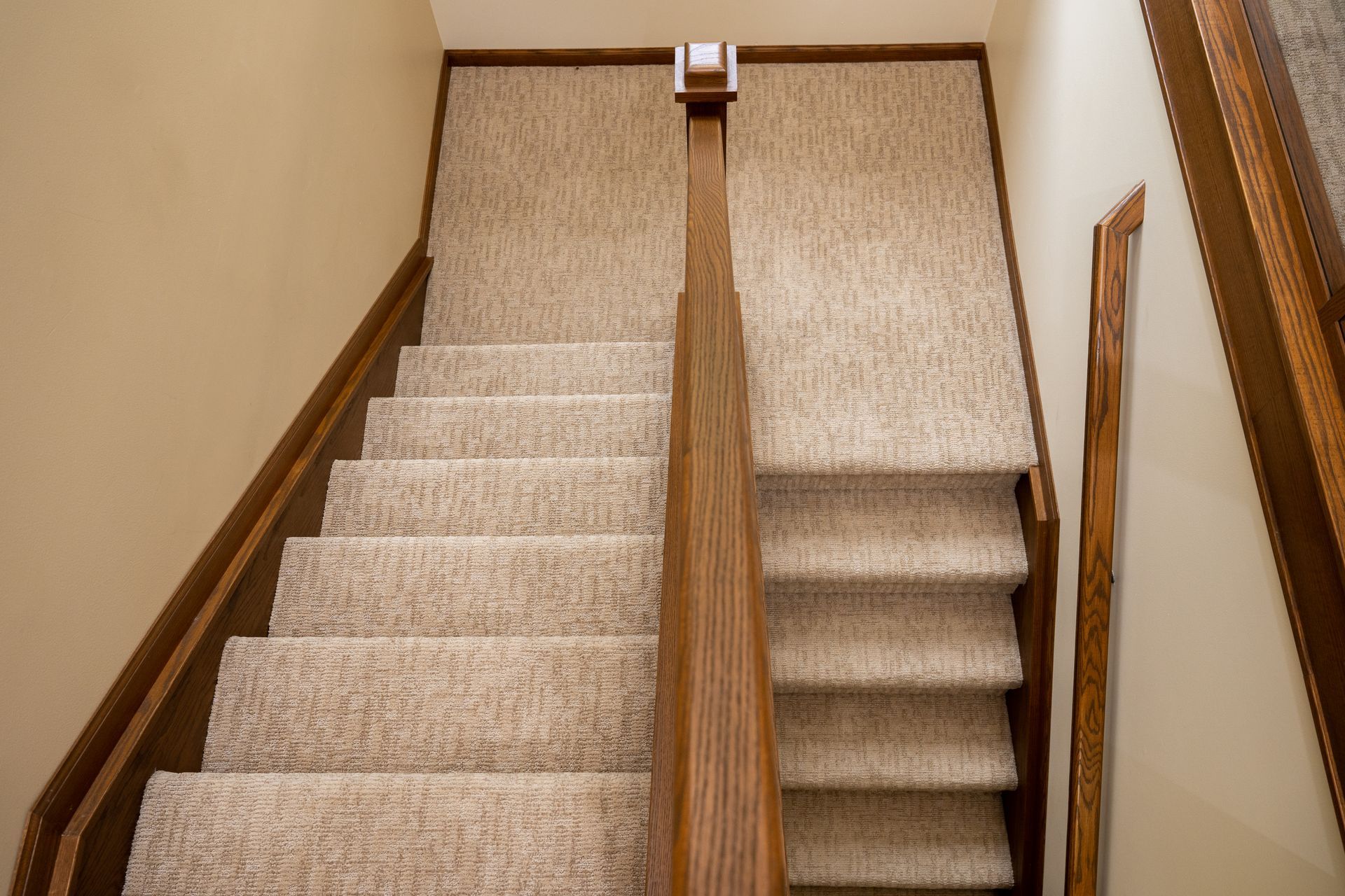 Top-down view of a carpeted stairway with beige walls and wooden handrails.