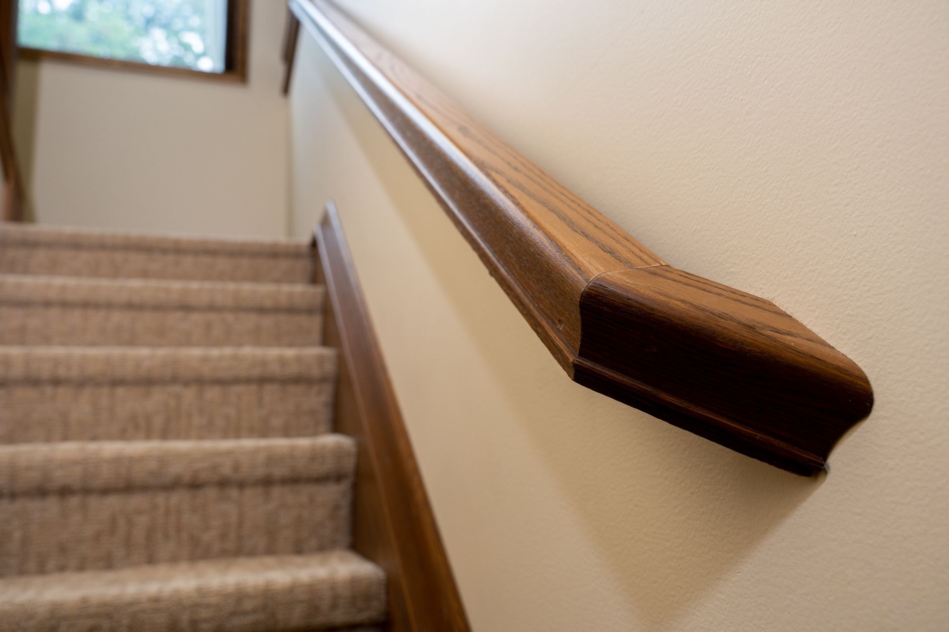 Staircase with beige carpet and a wooden handrail along a cream-colored wall