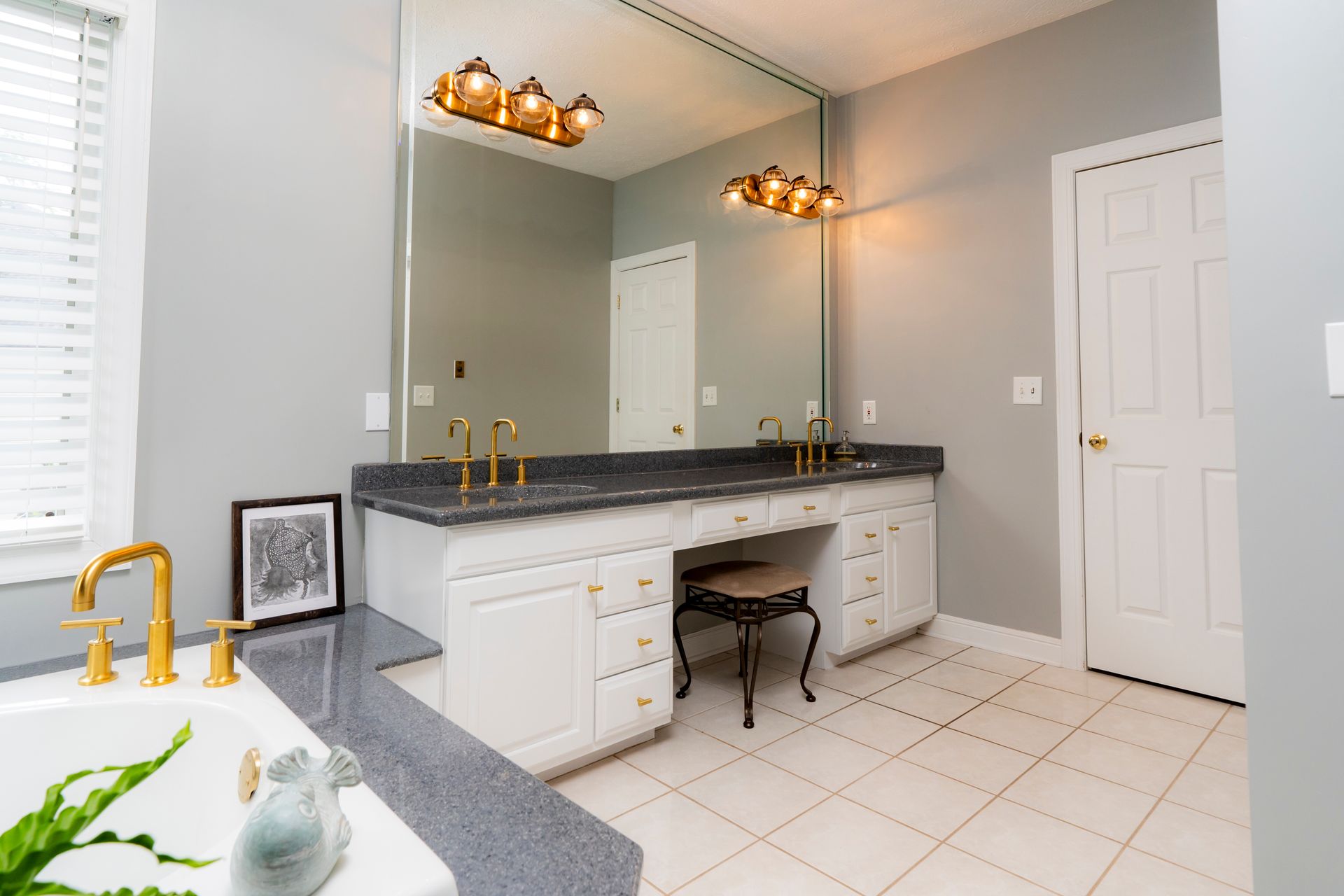 Bright modern bathroom with double vanity, large mirror, gold faucets, and white tile floor