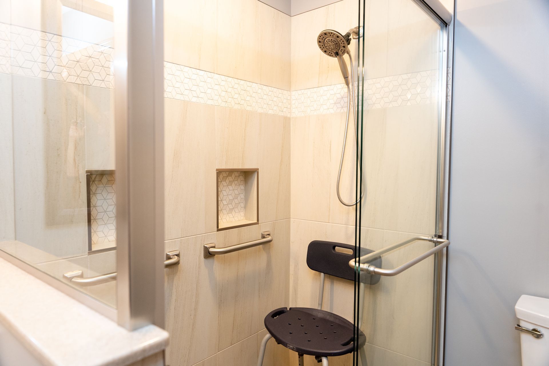 Accessible shower with grab bars, fold-down seat, handheld showerhead, and built-in wall niches.