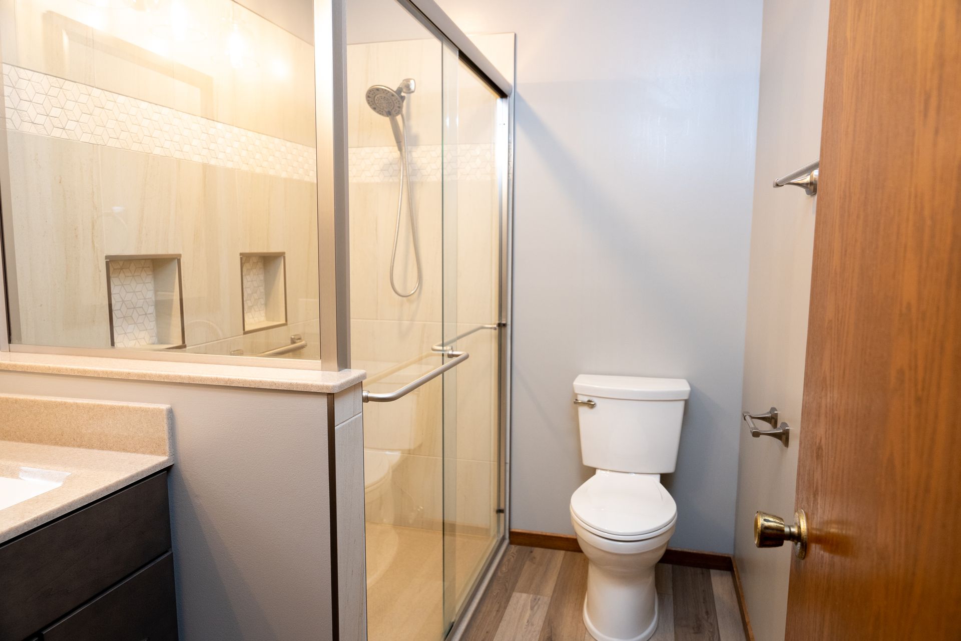 Small bathroom with a glass shower, toilet, sink counter, and wood door.