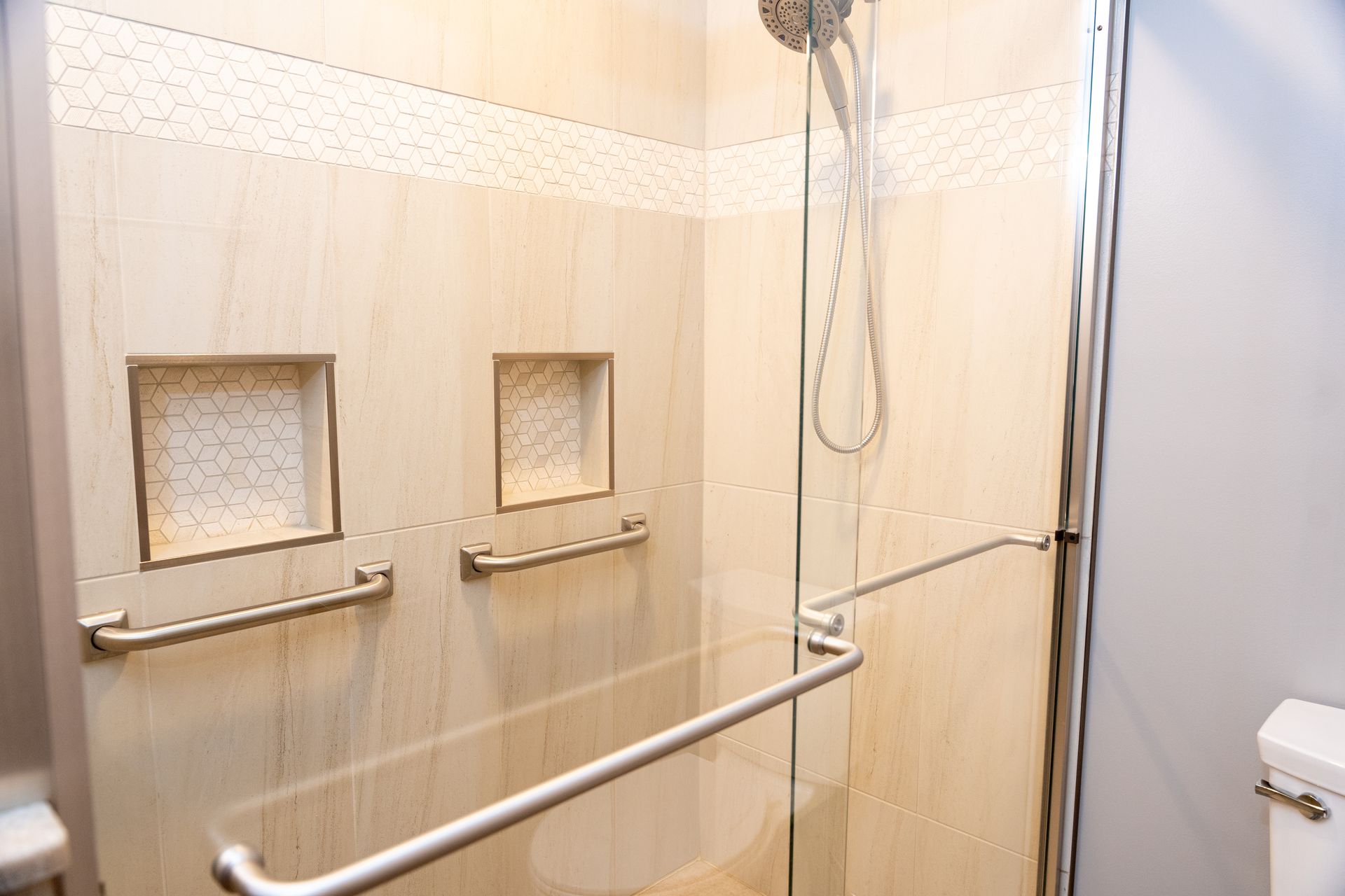 Accessible shower stall with grab bars, built-in shelves, and a handheld showerhead