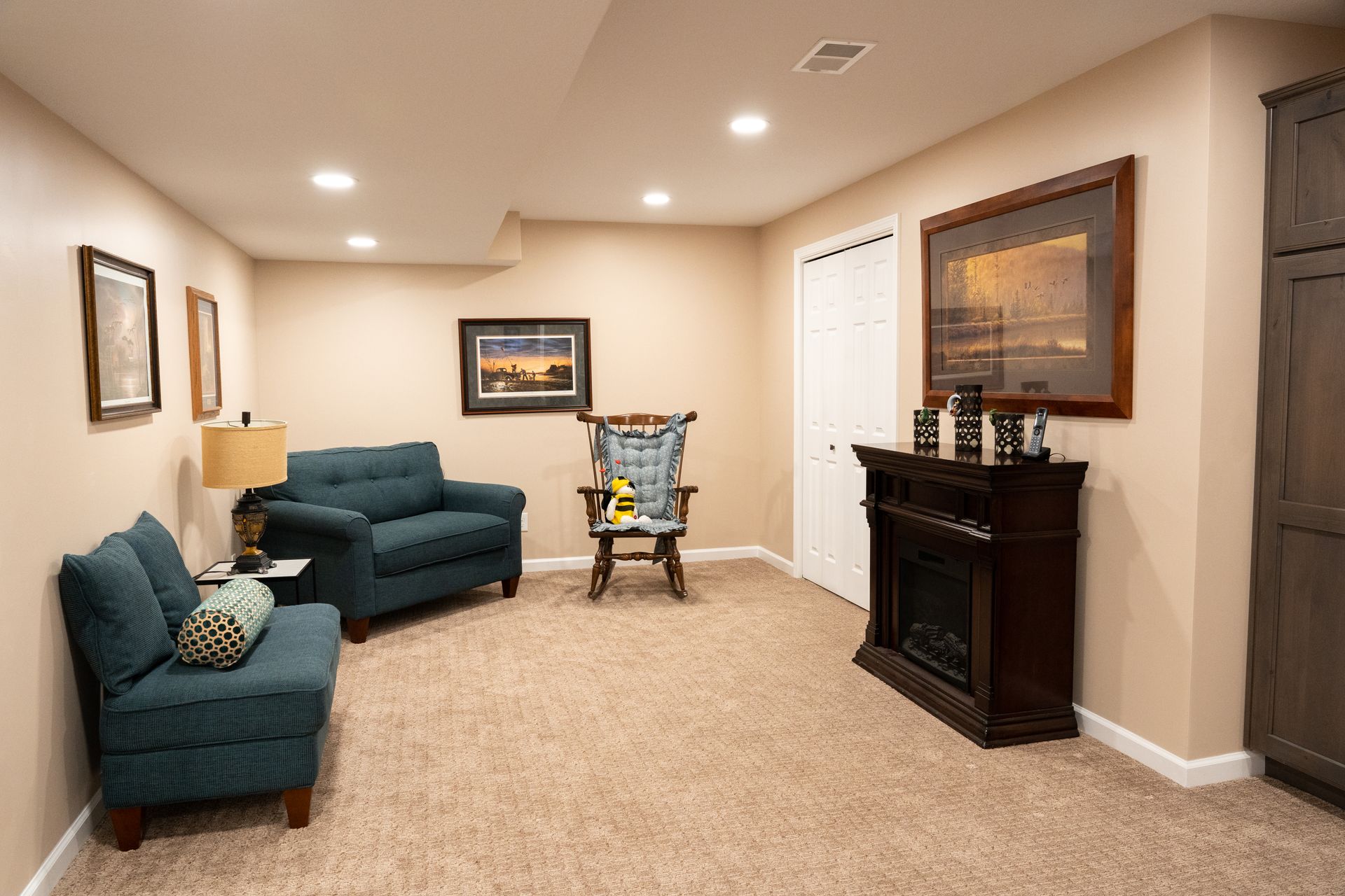 Basement living room with teal chairs, carpet, fireplace, and a baby walker near the back wall