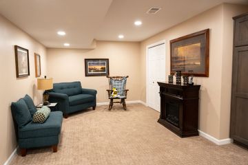 Basement living room with teal chairs, carpet, fireplace, and a baby walker near the back wall