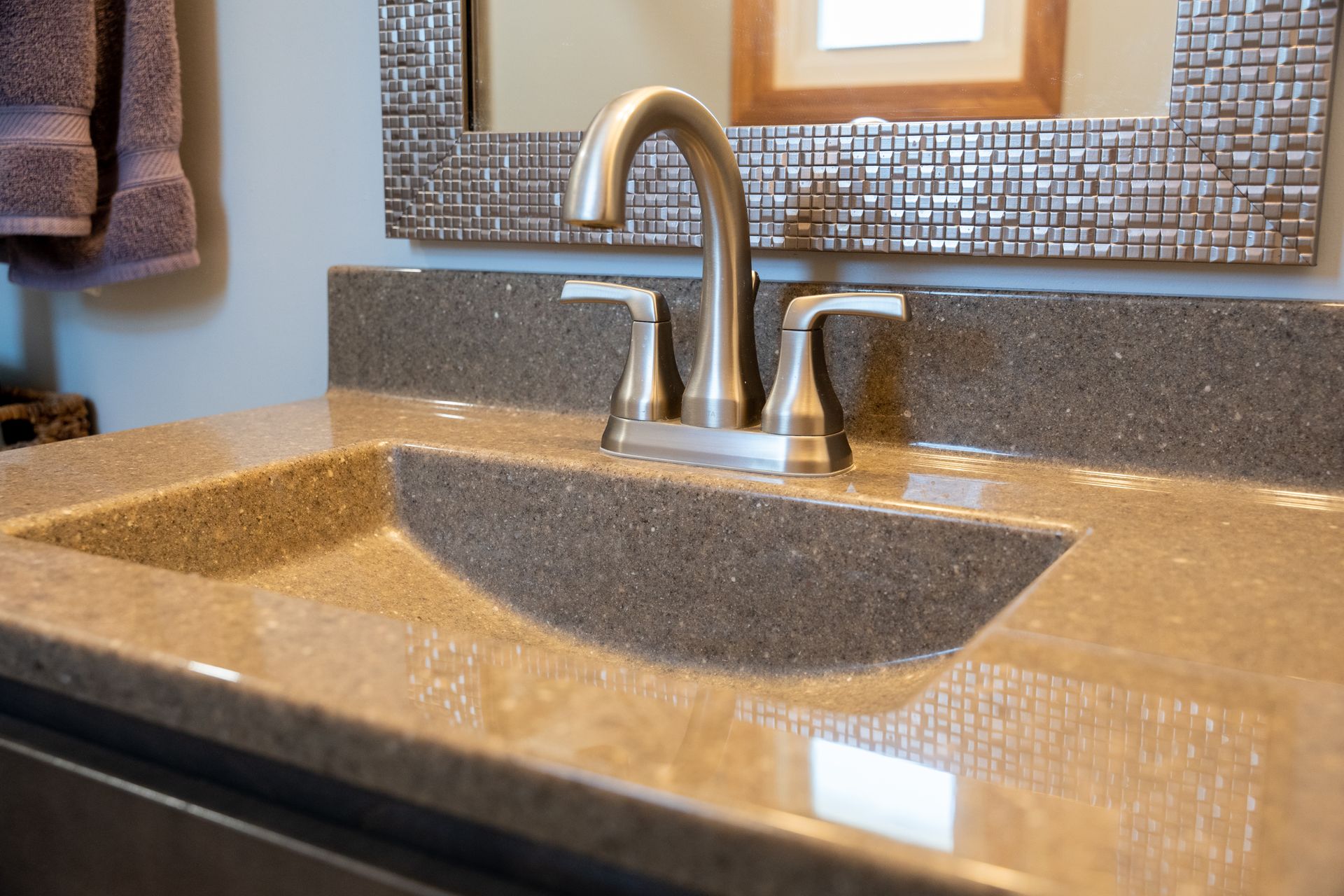 Granite bathroom sink with chrome faucet and mosaic tile backsplash near a window