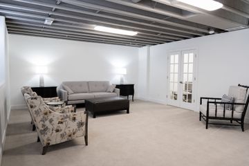Spacious living room with beige sofa, floral chairs, lamp, carpet, and white walls with exposed ceiling beams