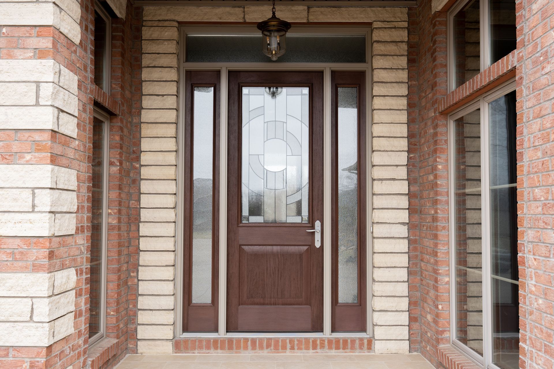 Front entrance with a brown wooden door, frosted glass panels, and brick framing under a covered porch