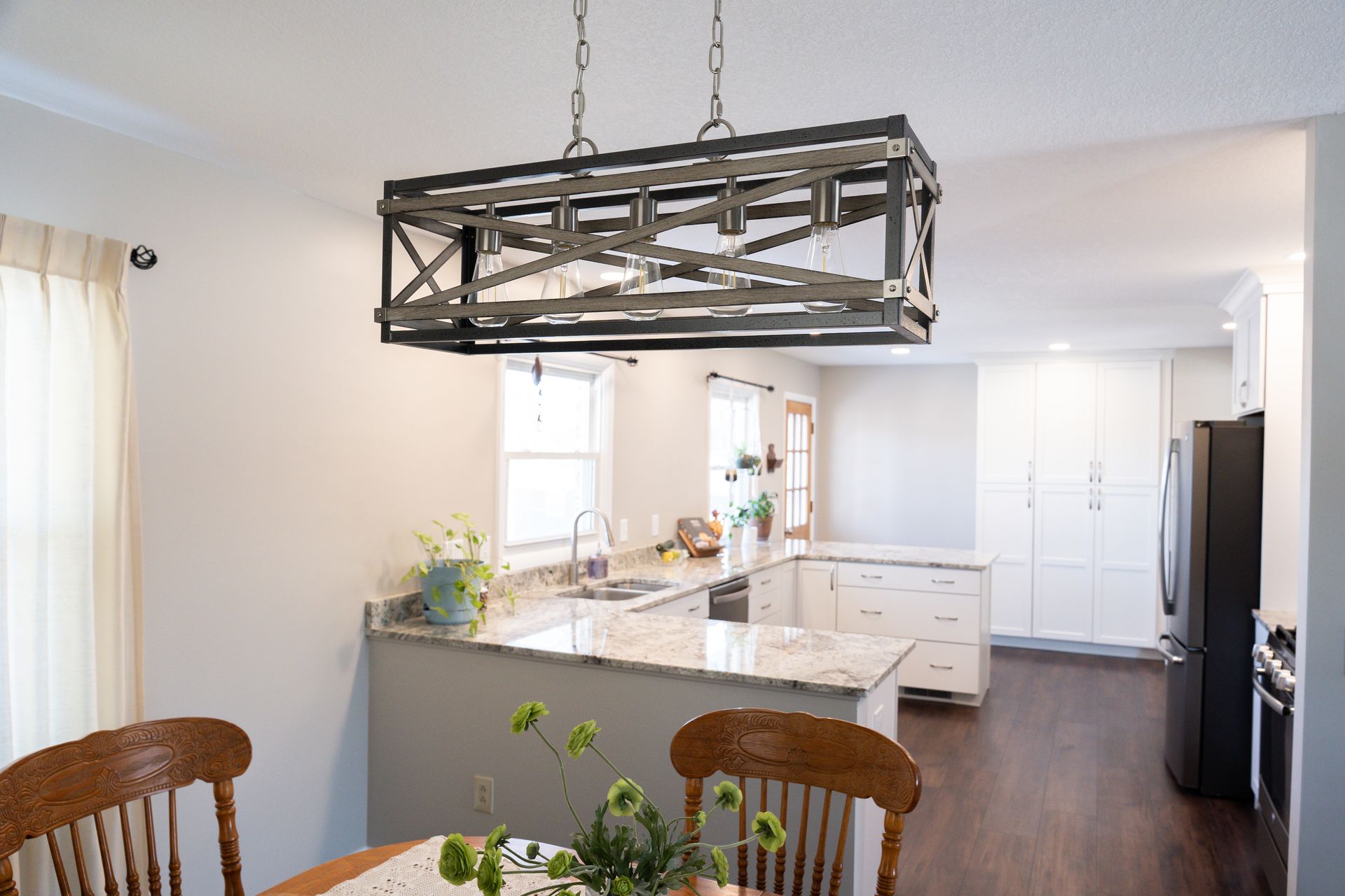 Bright kitchen with large island, white cabinets, dark floor, and hanging rectangular light above dining table